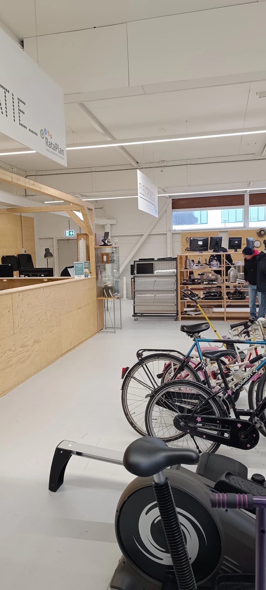 Winkelinterieur met houten balie, houten stellingen met electronica, zwarte metalen rekken en fietsen op de vloer