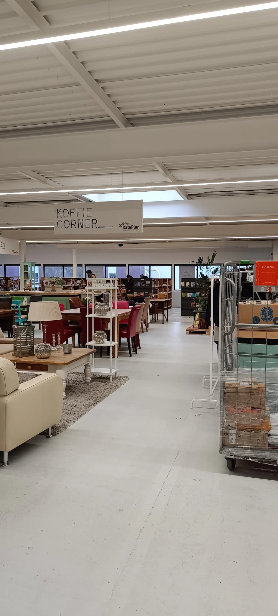 Winkelvloer met zithoeken, tafels, stoelen en boeken in een kringloopwinkel, met 'Koffie Corner' aangegeven