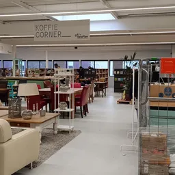Winkelvloer met zithoeken, tafels, stoelen en boeken in een kringloopwinkel, met 'Koffie Corner' aangegeven