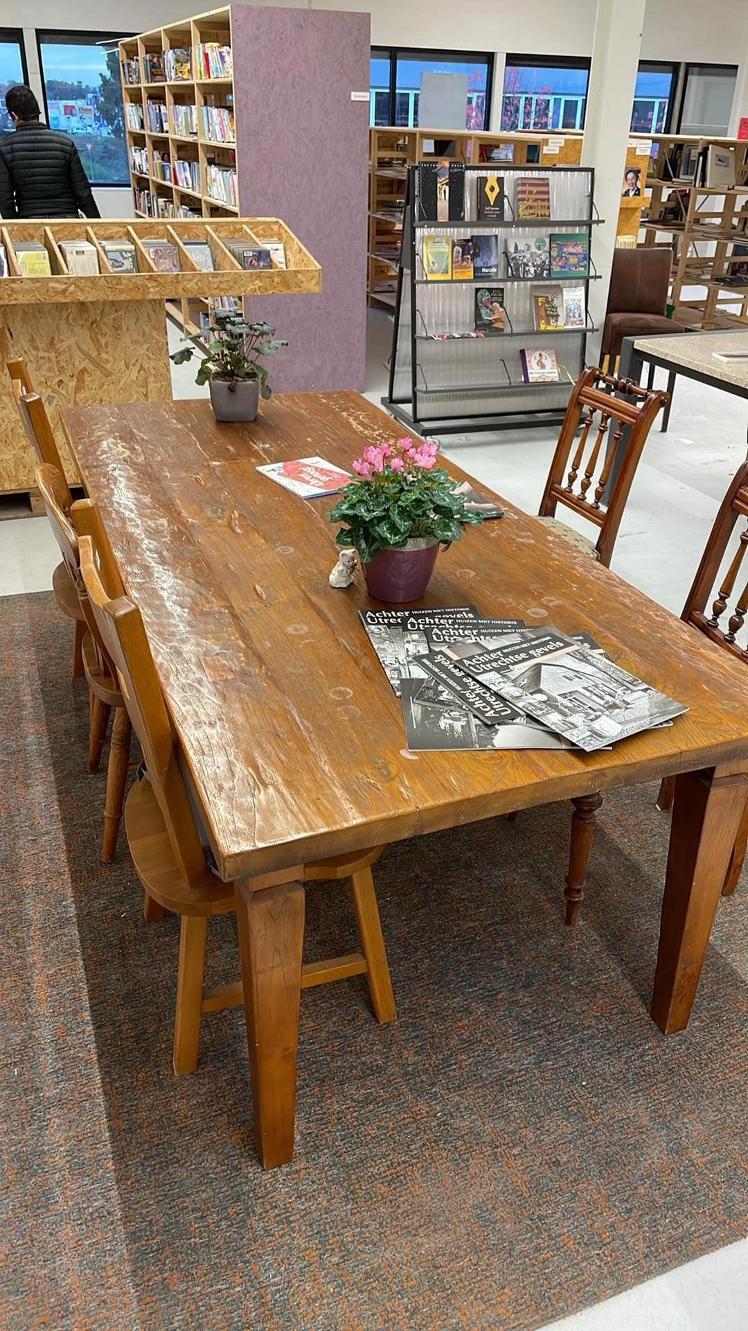 Houten eettafel met stoelen, roze bloemen in pot en tijdschriften op tafelblad