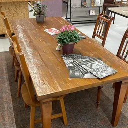 Houten eettafel met stoelen, roze bloemen in pot en tijdschriften op tafelblad