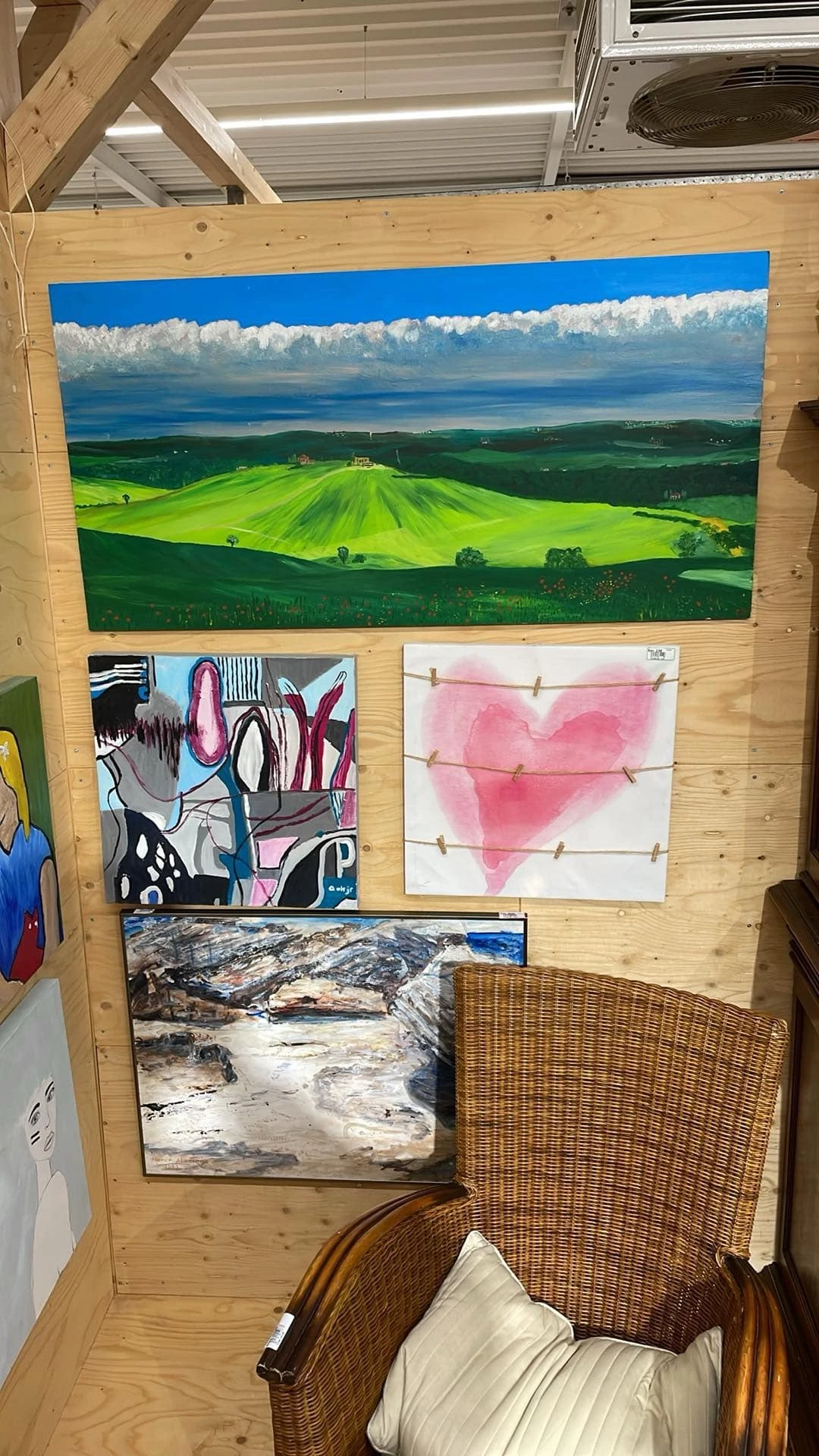 Kunstwerken aan houten wand: groen landschap, abstract schilderij, roze hartmotief en berglandschap