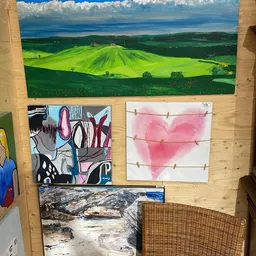 Kunstwerken aan houten wand: groen landschap, abstract schilderij, roze hartmotief en berglandschap