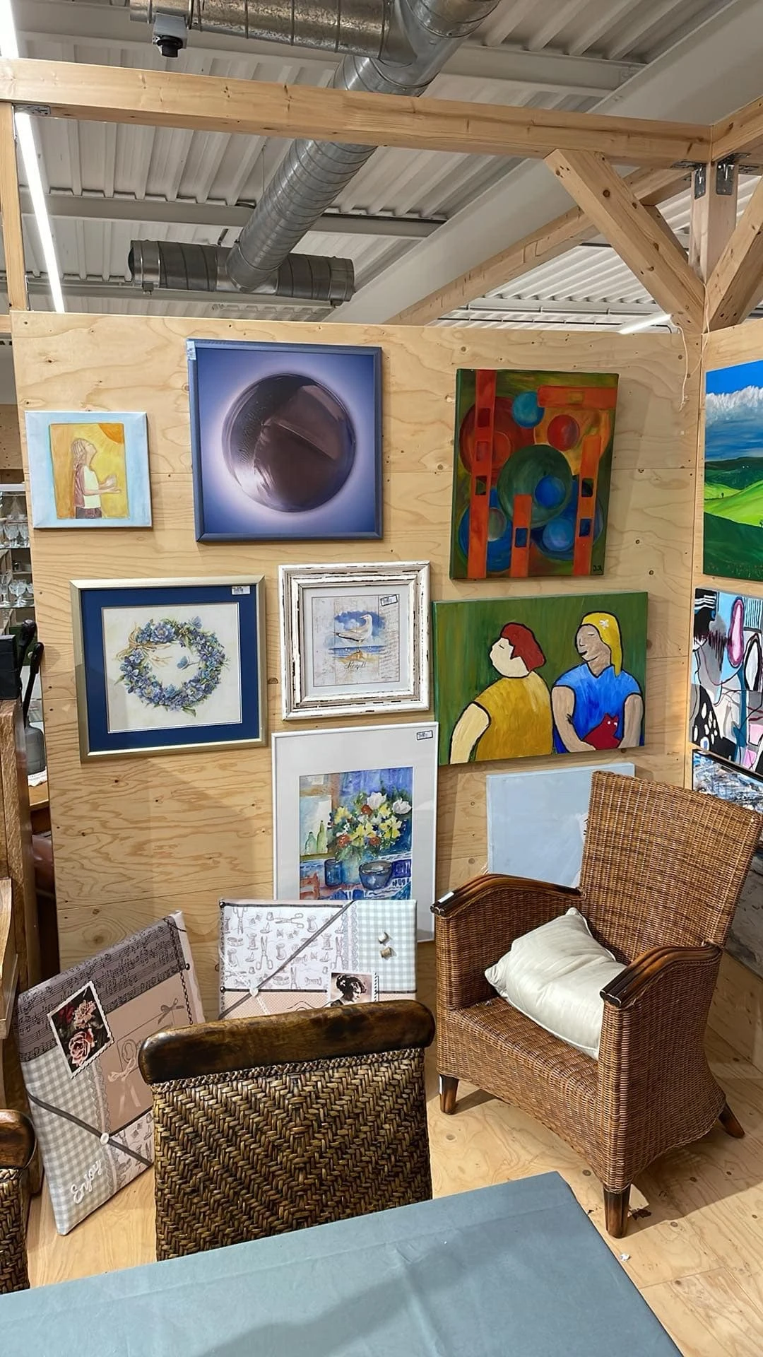 Verzameling schilderijen en kunstwerken uitgestald aan houten wand in kringloopwinkel