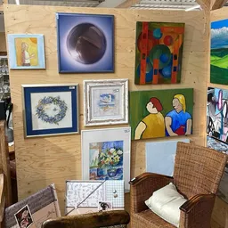 Verzameling schilderijen en kunstwerken uitgestald aan houten wand in kringloopwinkel