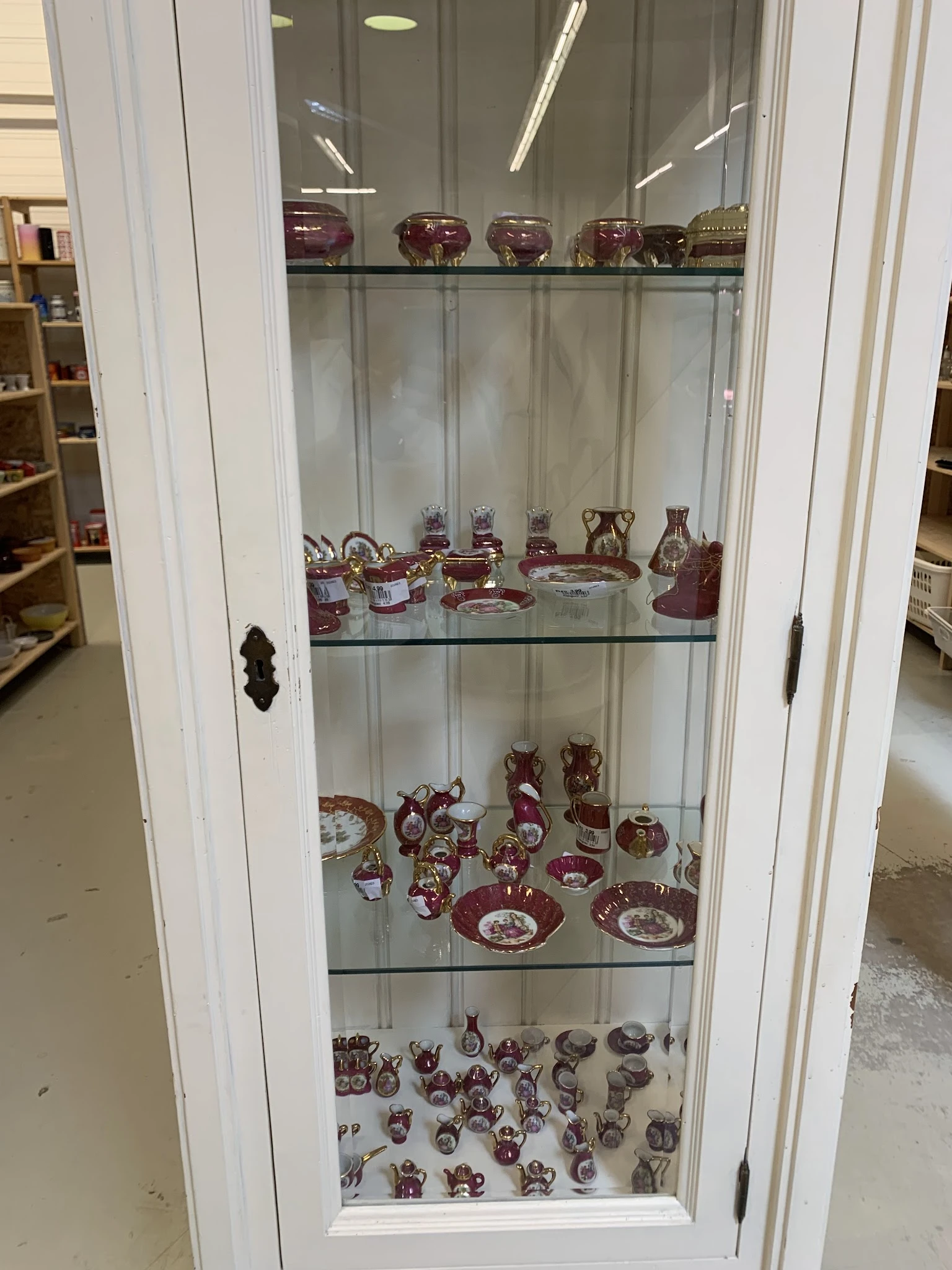 Glazen vitrinekast met rood-witte decoratieve serviesgoed en kandelaars op twee legels