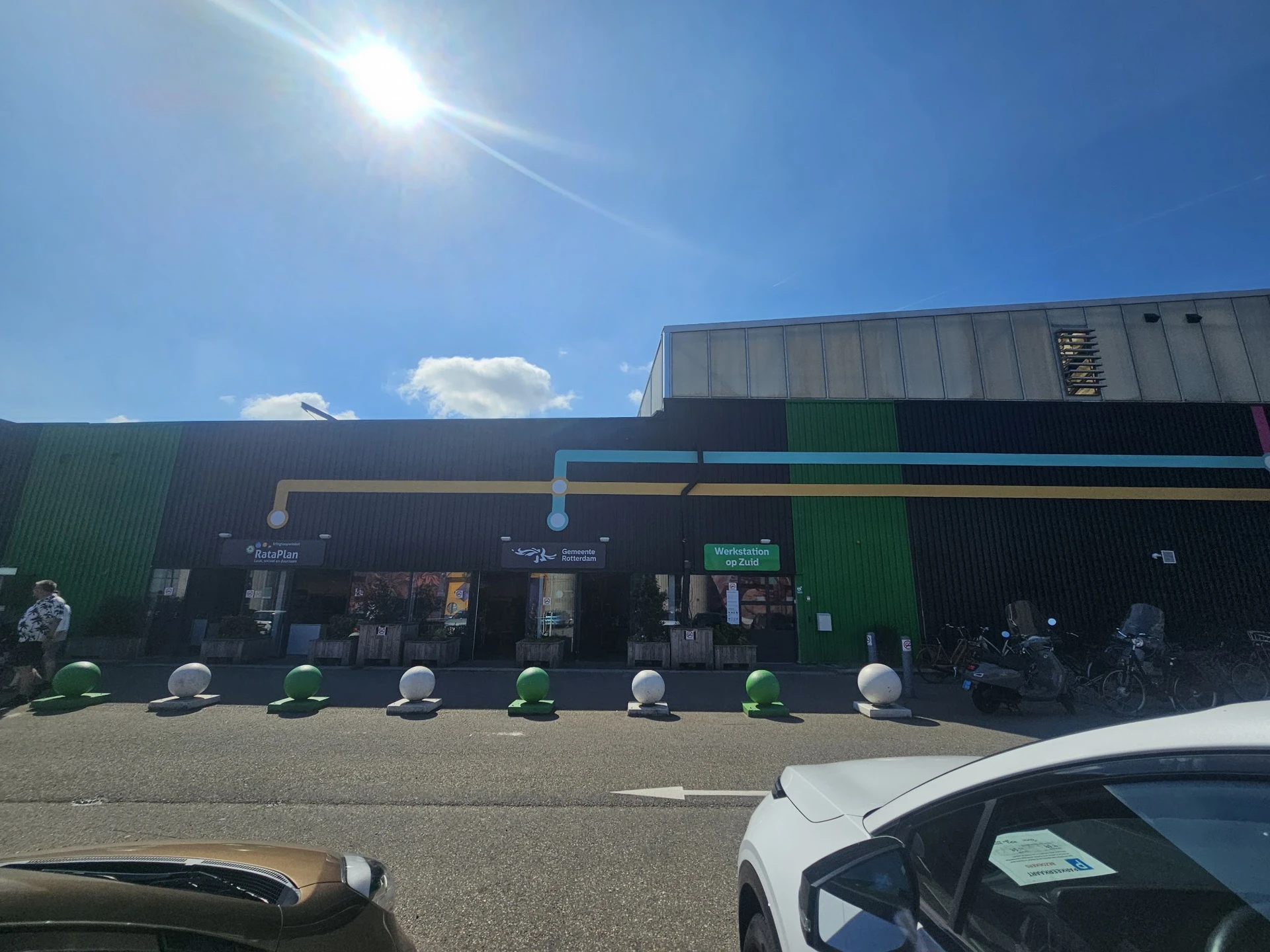 Voorgevel van kringloopwinkel met groene en donkerblauwe gevelsectie, blauwe luifel en witte bolletjes langs de ingang