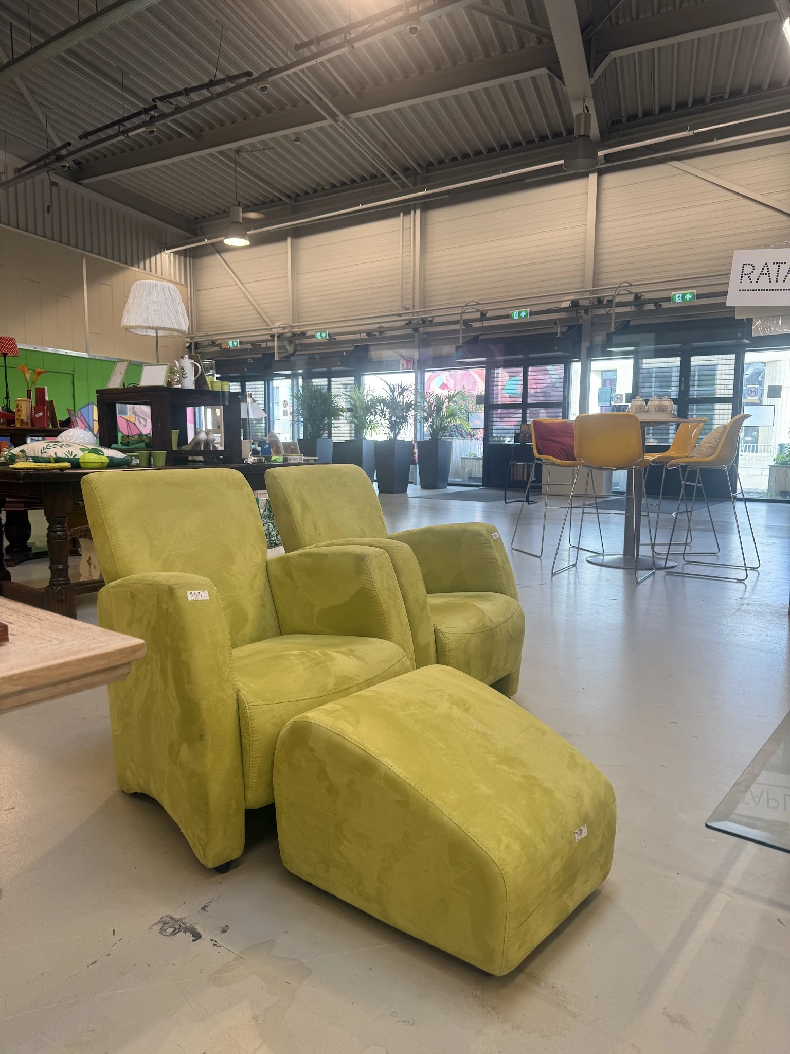 Winkelvloer met gele fauteuils en voetenbankje, stellingen en diverse meubels in het interieur van de kringloopwinkel
