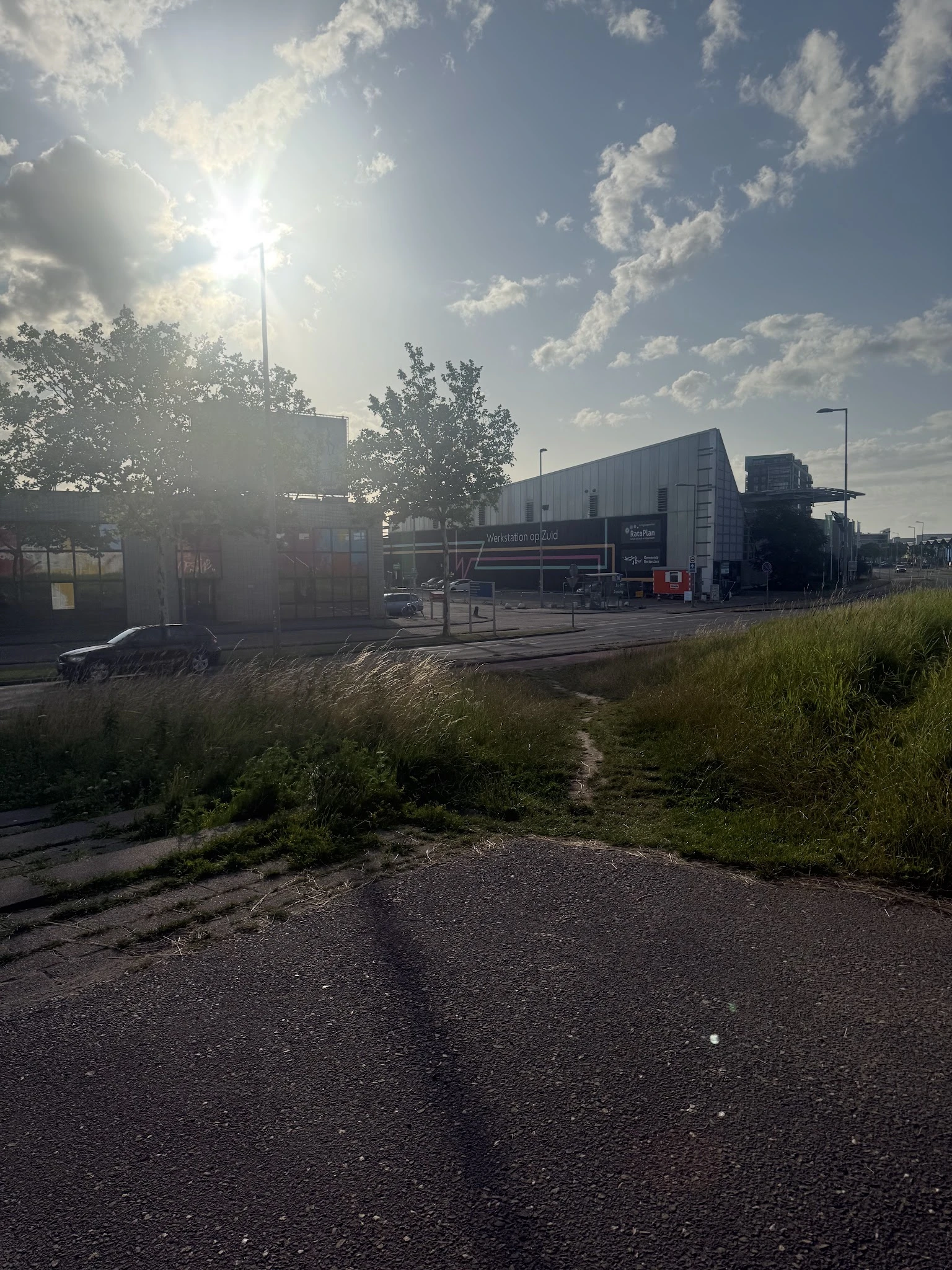 Extern industrieel terrein met kringloopwinkelgebouw, auto en groen, tegen hemel met wolken