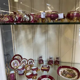 Glaskasten met bordeauxrood serviesgoed en decoratieve items op gouden standaards