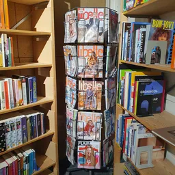 Draaiende display met magazines en boeken, omgeven door houten stellingen met dvd's, boeken en ander tweedehands assortiment