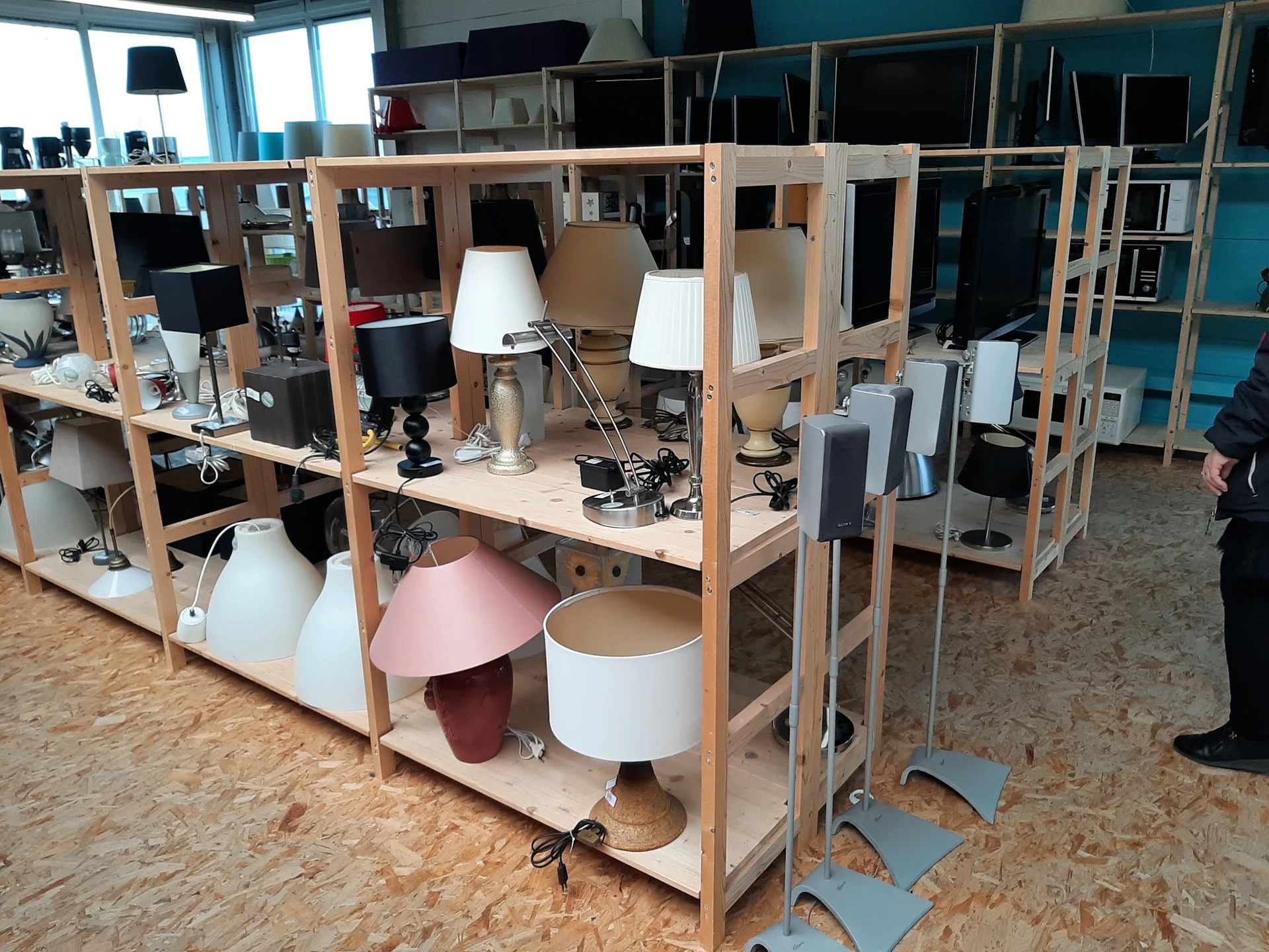 Winkelinterieur met houten stellingkasten, bureaulampen, speakers en diverse tweedehands voorwerpen op een kurken vloer