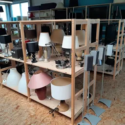 Winkelinterieur met houten stellingkasten, bureaulampen, speakers en diverse tweedehands voorwerpen op een kurken vloer