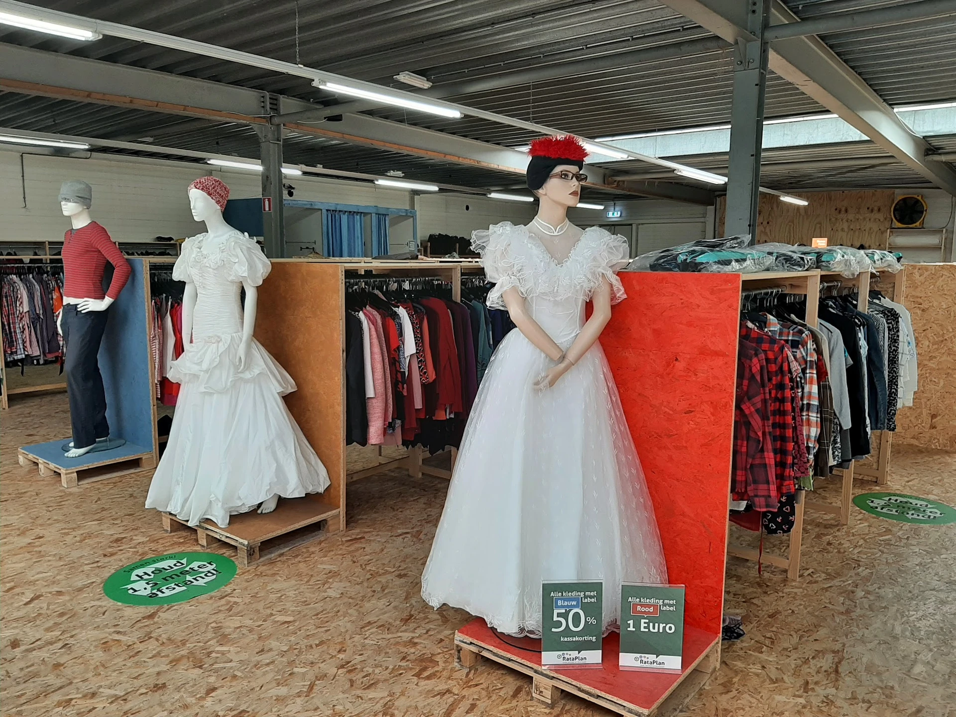 Kledingrekken met jurken, jassen en andere tweedehands kleding in de winkel, met etalagepoppen in witte jurken