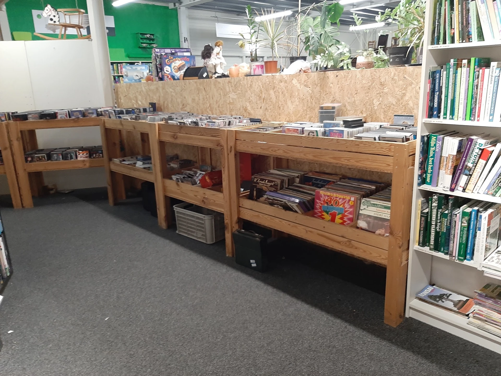 Winkelinterieur met houten vitrinekasten vol dvd's, cd's en spellen, rechts boekenkasten, groene muur op achtergrond