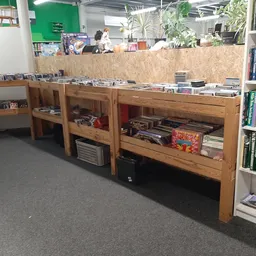 Winkelinterieur met houten vitrinekasten vol dvd's, cd's en spellen, rechts boekenkasten, groene muur op achtergrond