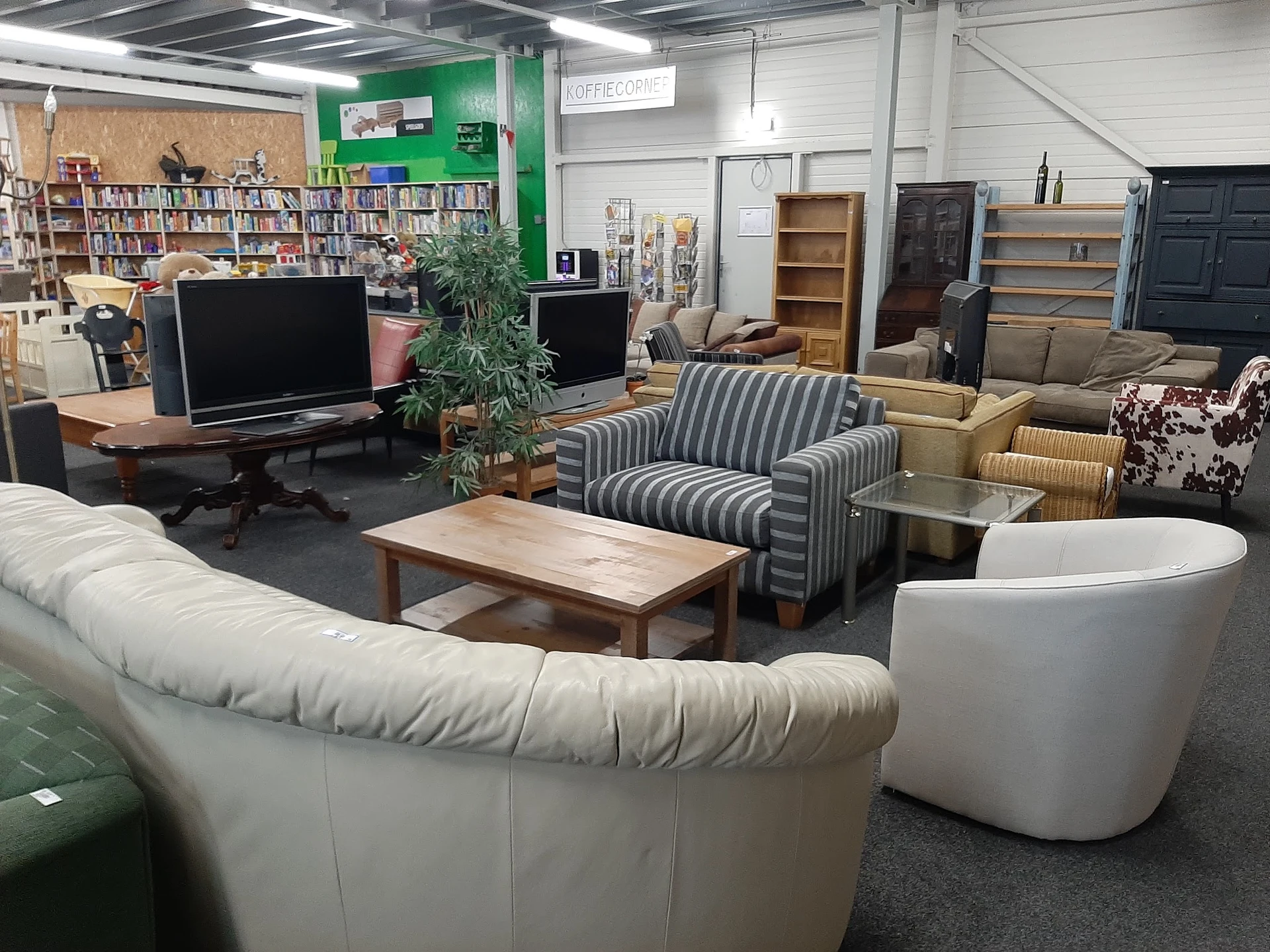 Winkelvloer met zithoeken, banken, fauteuils, salontafel, computers en boekenkasten op de achtergrond