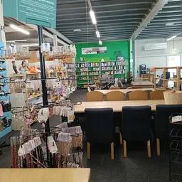 Winkelinterieur met boekenkasten, displayrekken met huishoudwaar, zittinghoek met houten stoelen en tafel