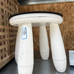 Witte kruk of tafelblad met drie poten en zwart rand, voorzien van winkelsticker
