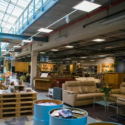 Ruim winkelinterieur met bruine stoelen en fauteuils, verlichte vitrines met spullen op achtergrond, industrieel plafond met 