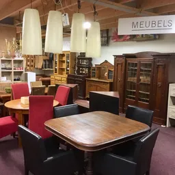 Winkelvloer met uitgestalde meubels: eettafel met zwarte stoelen, rode fauteuils, kasten en hanglampen
