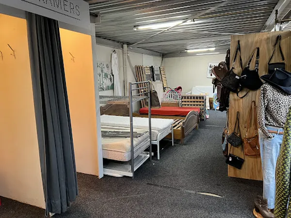 Winkelinterieur met bedden, stapelbedden, kledingrekken en diverse tweedehands spullen uitgestald