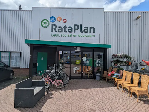 Voorgevel van kringloopwinkel met groene luifel, ingang, naam RataPlan en daarnaast gebruikte fietsen en houten meubels buite