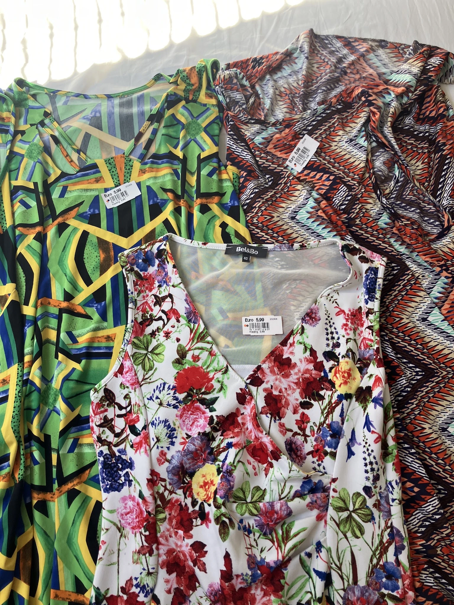 Rekken met tweedehands kleding met verschillende patronen en prints, waaronder bloemendessin en geometrische patronen