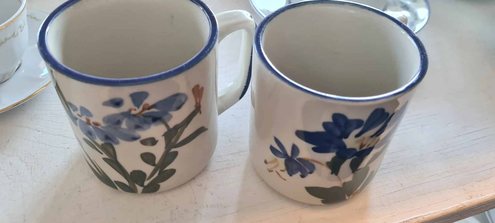 Twee witte aardewerken mokken met blauwe rand en bloemendecoratie