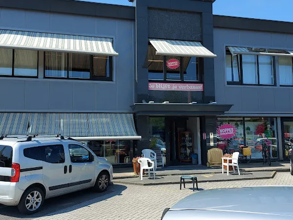 Gevel van kringloopwinkel RataPlan met etalages, terrasstoel en geparkeerde auto