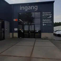 Ingang van kringloopwinkel met donkerblauw gevel, glazen deuren en wegwijzers voor doneren en ophalen