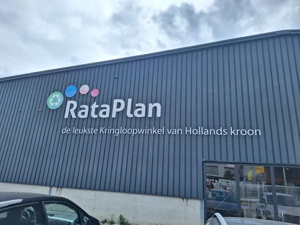 Gevel van kringloopwinkel RataPlan met logo en winkelnaam op grijze golfplaten wand