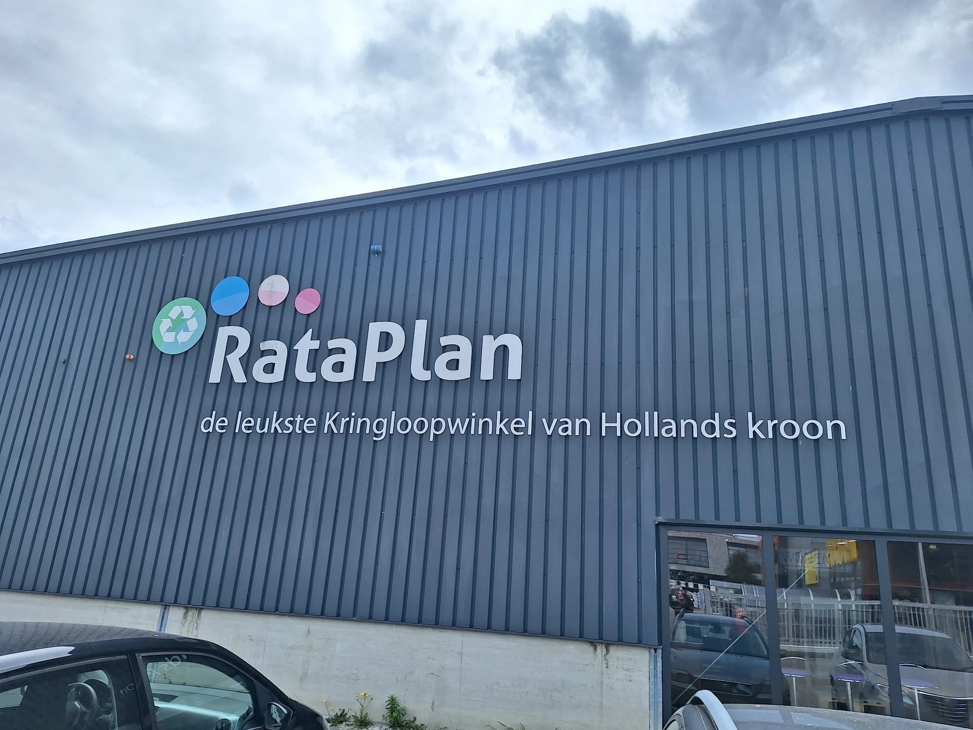 Gevel van kringloopwinkel RataPlan met logo en winkelnaam op grijze golfplaten wand