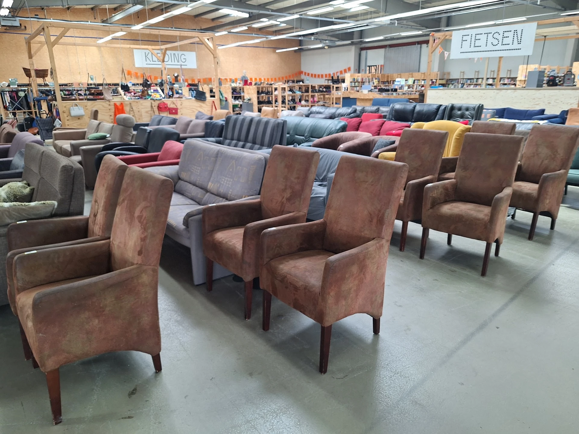 Uitgestalde fauteuils en stoelen in verschillende kleuren en stijlen in de kringloopwinkel