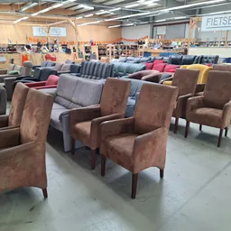 Uitgestalde fauteuils en stoelen in verschillende kleuren en stijlen in de kringloopwinkel