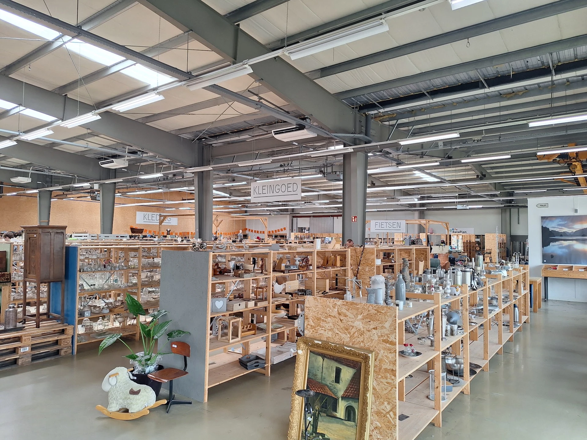 Ruime winkelvloer met houten stellingen en kasten vol tweedehandsartikelen, industrieel plafond met verlichting