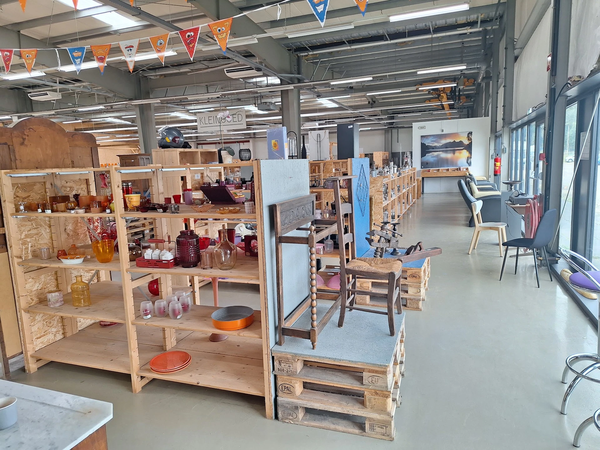 Winkelvloer met houten stellingen vol spullen, speelgoed en huishoudartikelen onder industrieel plafond