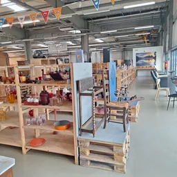 Winkelvloer met houten stellingen vol spullen, speelgoed en huishoudartikelen onder industrieel plafond
