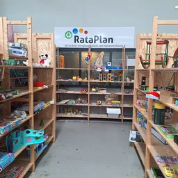 Winkelvloer met houten stellingen vol speelgoed, boeken en huishoudartikelen, RataPlan-bord zichtbaar