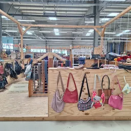 Uitgestalde tassen en handtassen aan houten display, met op de achtergrond meer tweedehands spullen in de kringloopwinkel