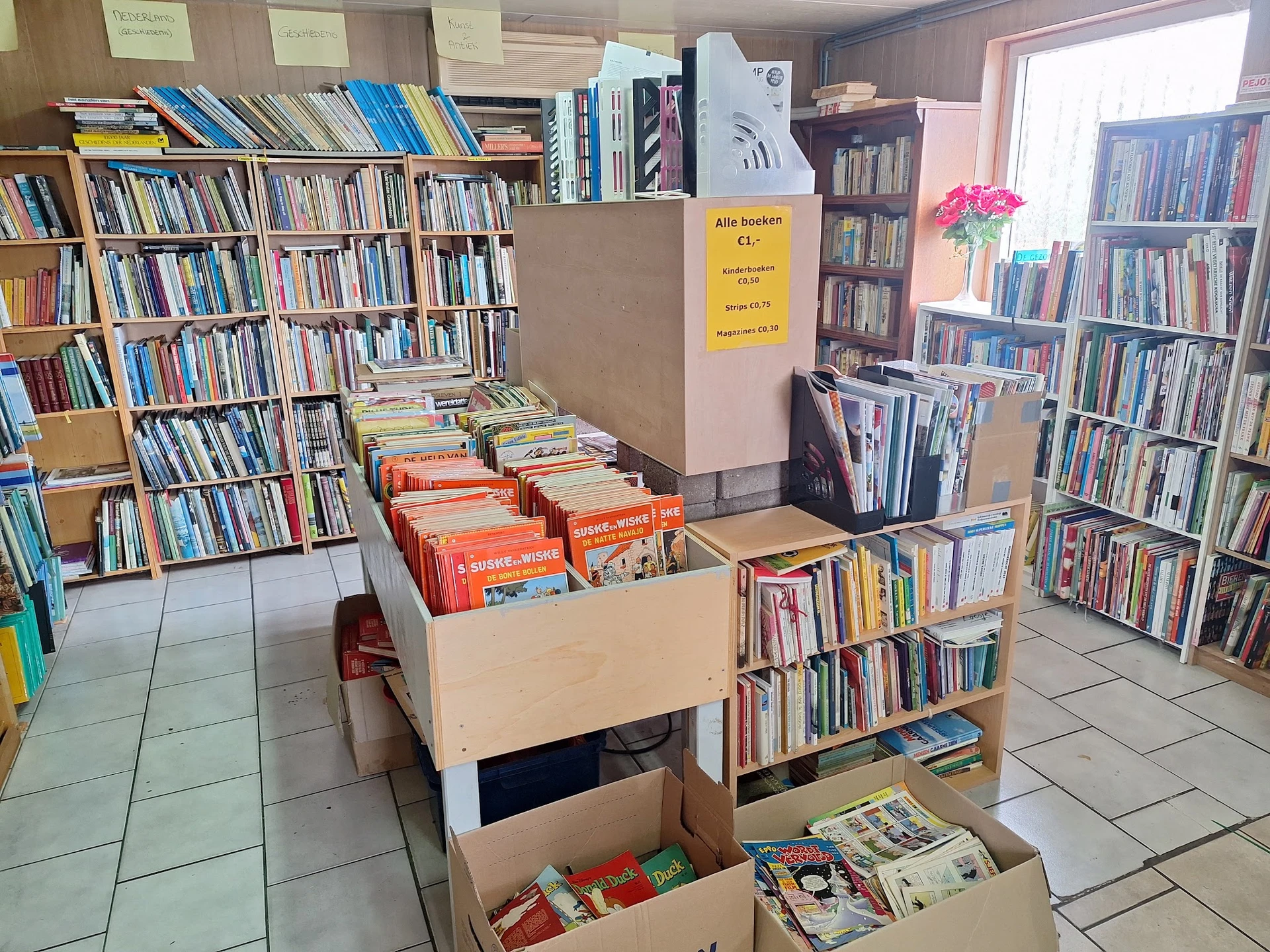Binnenaanzicht van kringloopwinkel met boekenkasten, stellingen vol boeken en kartonnen dozen met boeken op de vloer