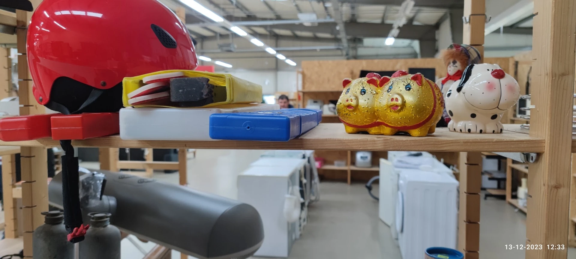 Verschillende tweedehands items op een houten plank: rode helm, gele speelgoedeendjes, gereedschap en huishoudelijke spullen