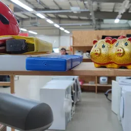 Verschillende tweedehands items op een houten plank: rode helm, gele speelgoedeendjes, gereedschap en huishoudelijke spullen