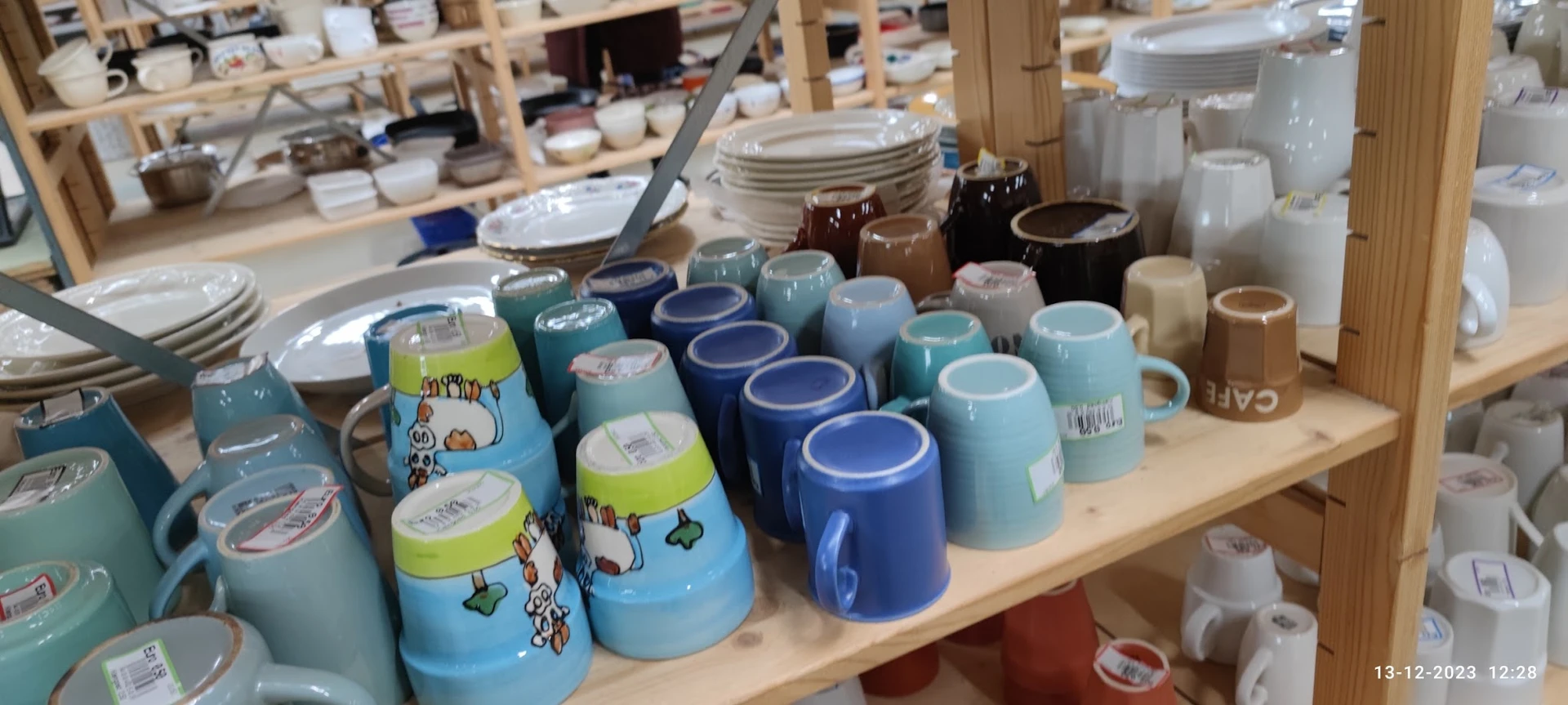 Rekken met servies en kopjes in verschillende kleuren, vooral blauwe en turquoise tinten, in de kringloopwinkel