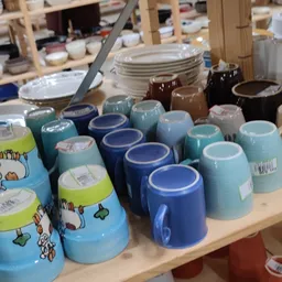 Rekken met servies en kopjes in verschillende kleuren, vooral blauwe en turquoise tinten, in de kringloopwinkel