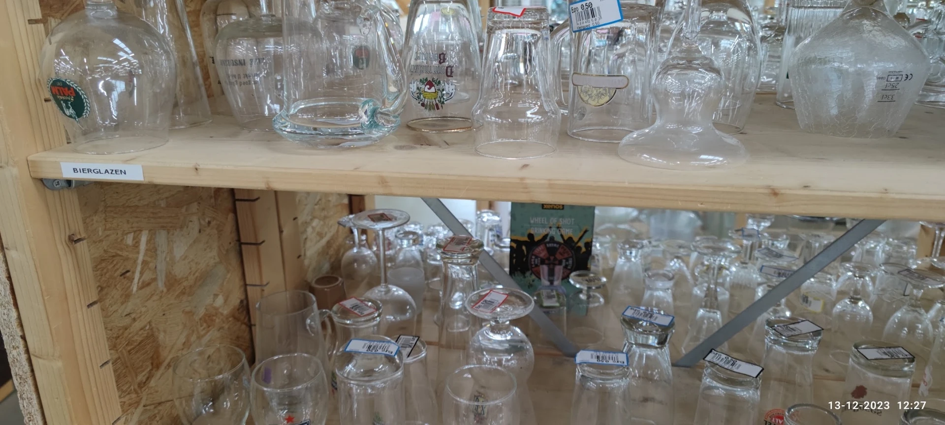 Twee schappen met glazen bekers, kannen en drinkglazen met prijskaartjes