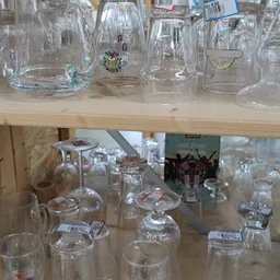 Twee schappen met glazen bekers, kannen en drinkglazen met prijskaartjes