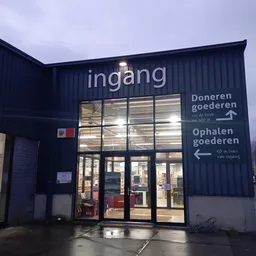 Avondfoto van de ingang van kringloopwinkel RataPlan met verlichte gevelreclame en bewegwijzering