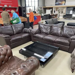 Bruine leren zitgroepen en fauteuils in een kringloopwinkel met rood accent op de achterwand