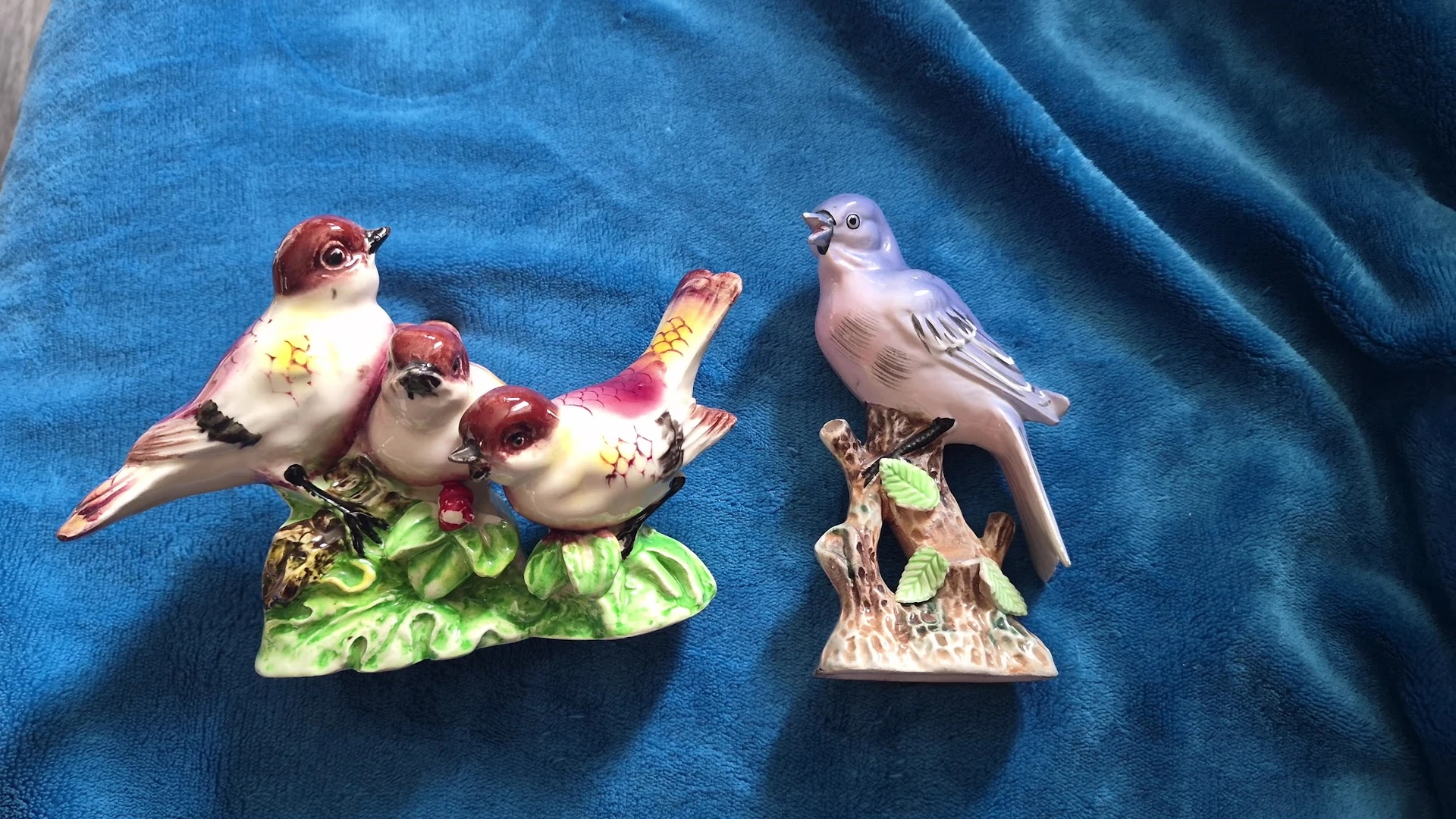 Twee porseleinen vogelbeeldjes op blauwe stof